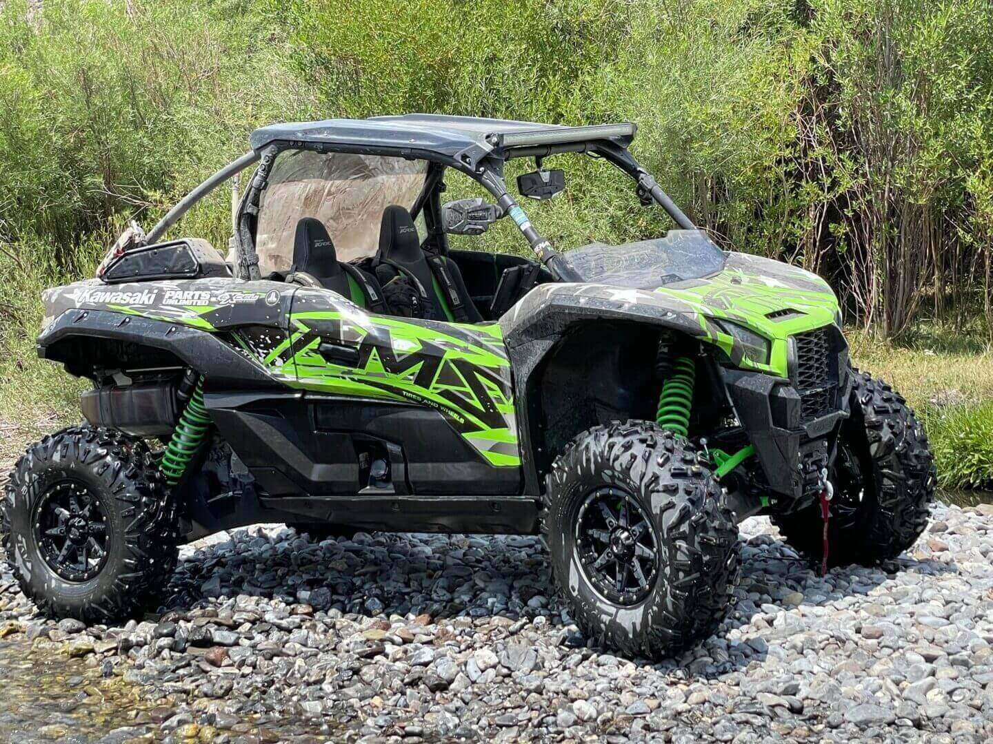 A green and black kawasaki teryx krx 1000 utility terrain vehicle parked on a rocky landscape with shrubs in the background.